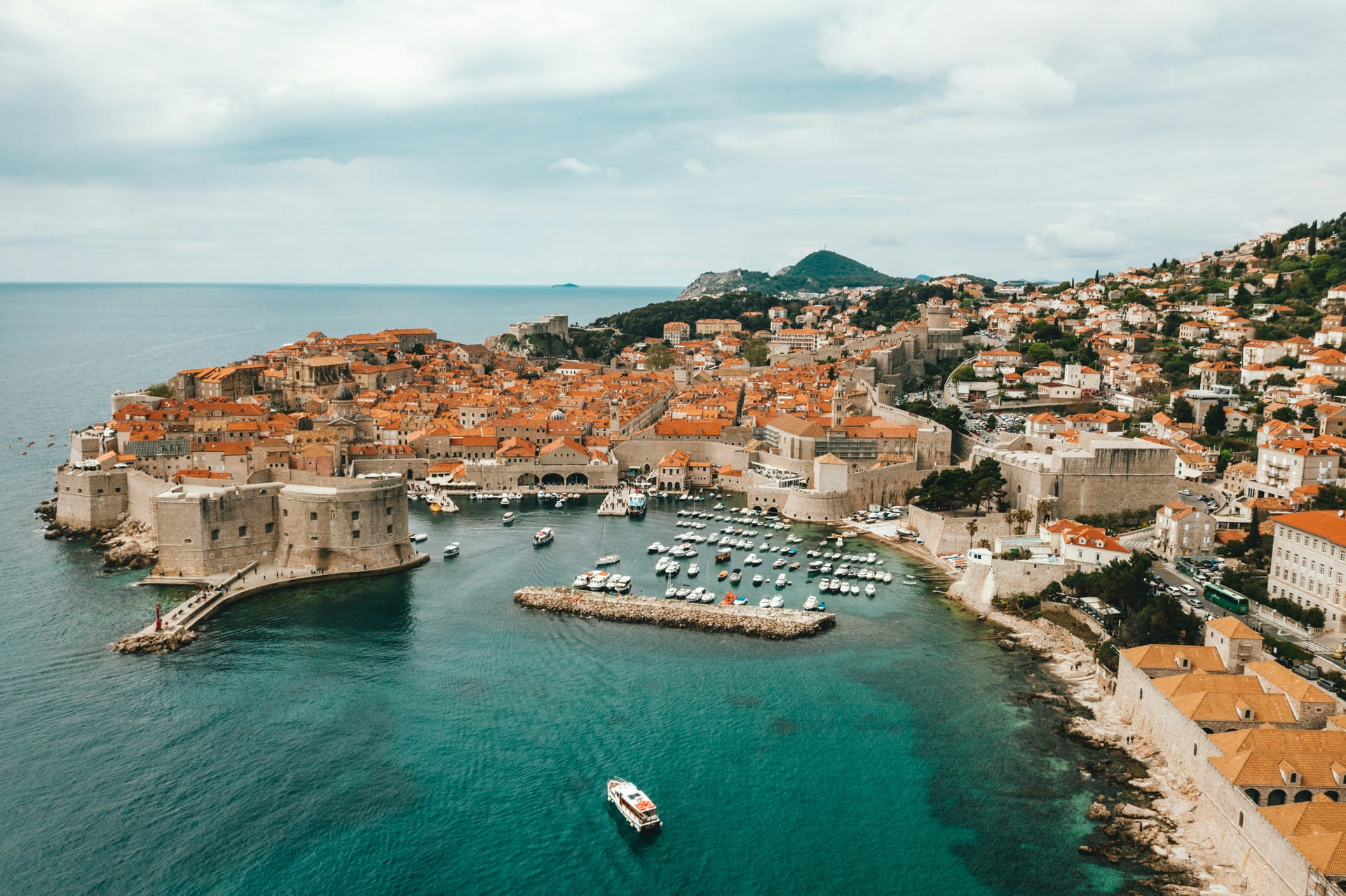 An aerial view of the walled Old Town of Dubrovnik with its orange rooftops jutting out into the blue Adriatic Sea.